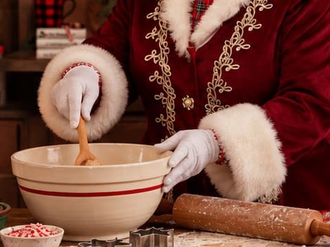 Mrs. Claus stirring dough in a red-striped mixing bowl