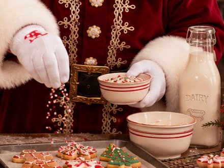 Santa shaking festive sprinkles over a tray of cookies